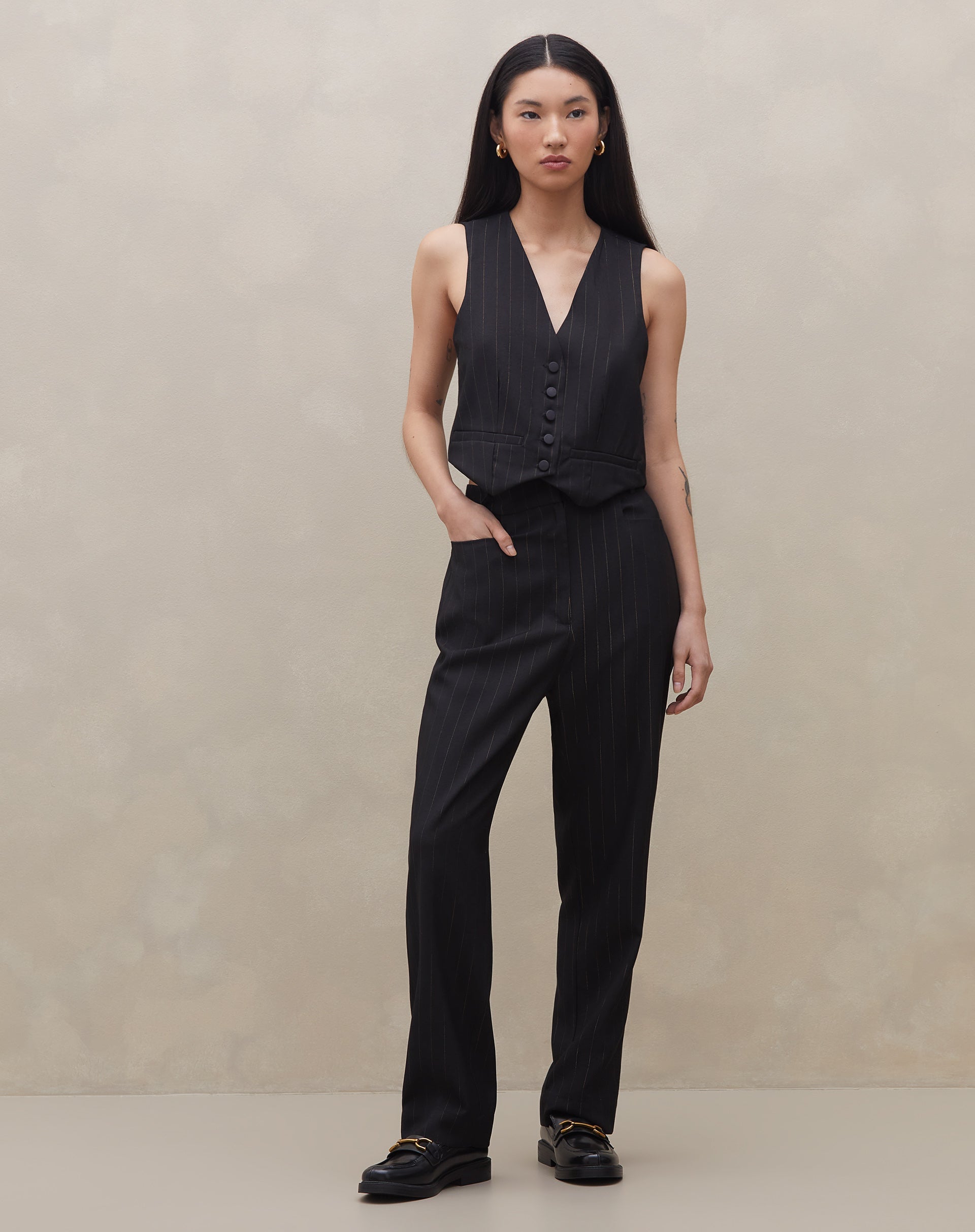 Modelo vestindo calça preta cropped com risca de giz e colete combinando, vista frontal.