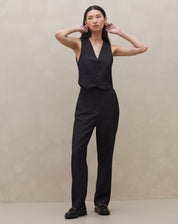 Modelo vestindo conjunto de calça e colete preto com risca de giz, vista lateral.