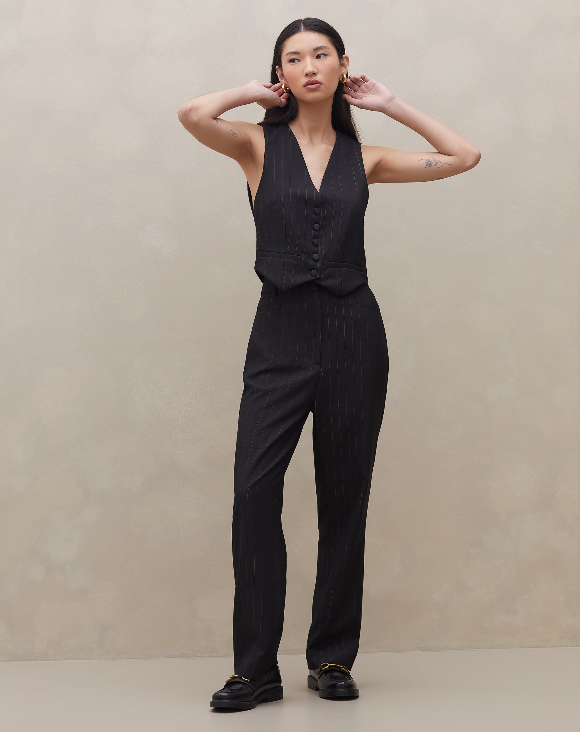 Modelo vestindo conjunto de calça e colete preto com risca de giz, vista lateral.