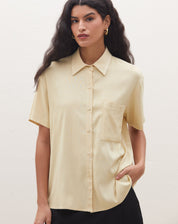 Detalhe da camisa manga curta com bolso em tom areia, mostrando o colarinho e fechamento com botões.