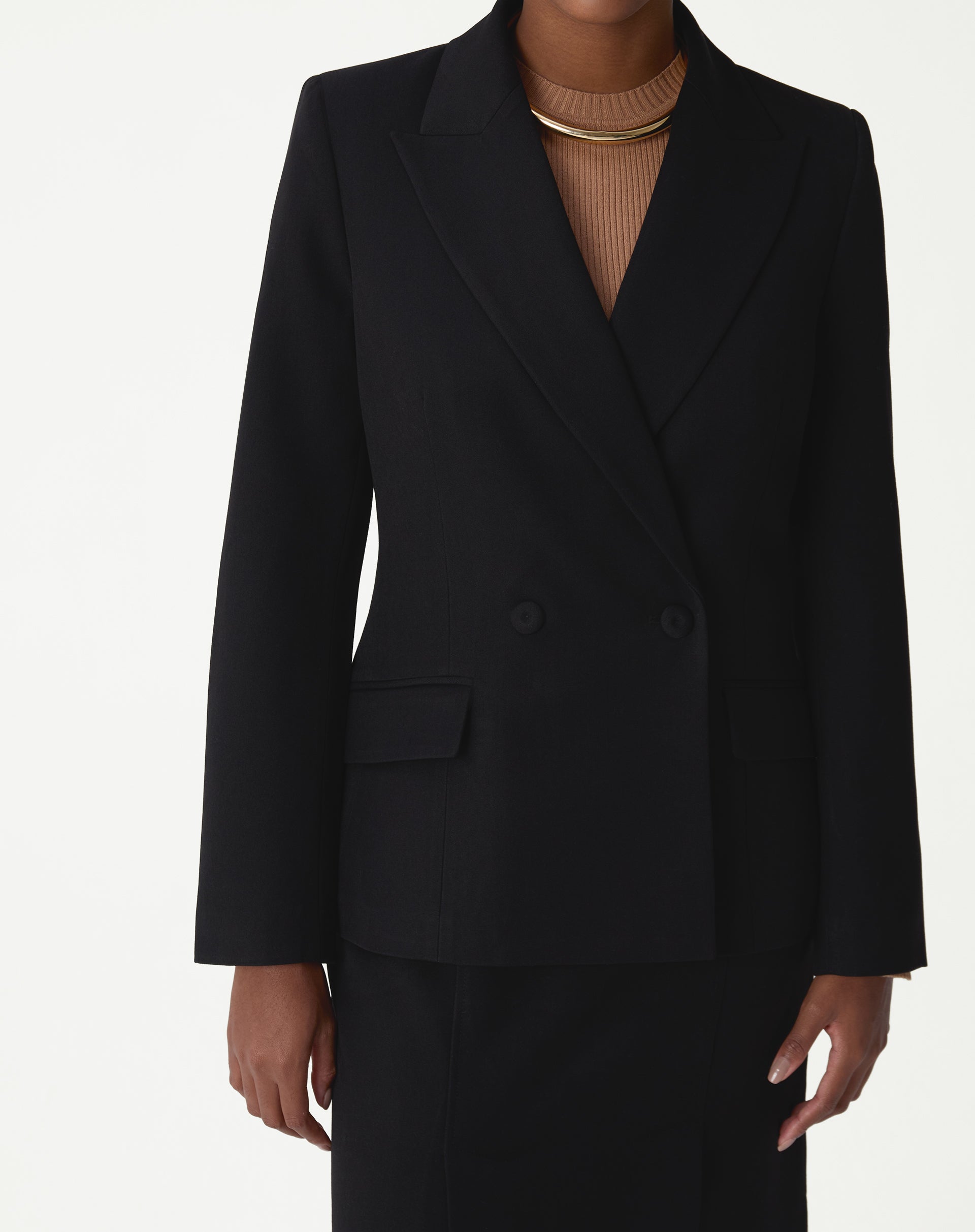 Vista frontal do blazer mostrando abotoamento duplo, bolsos com aba e botões revestidos em close médio