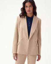 Modelo utilizando blazer bege slim de alfaiataria com abotoamento duplo e detalhes de bolsos com aba.