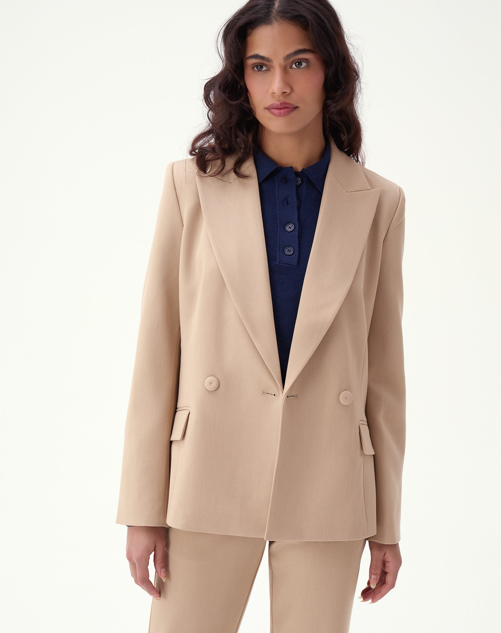 Modelo utilizando blazer bege slim de alfaiataria com abotoamento duplo e detalhes de bolsos com aba.