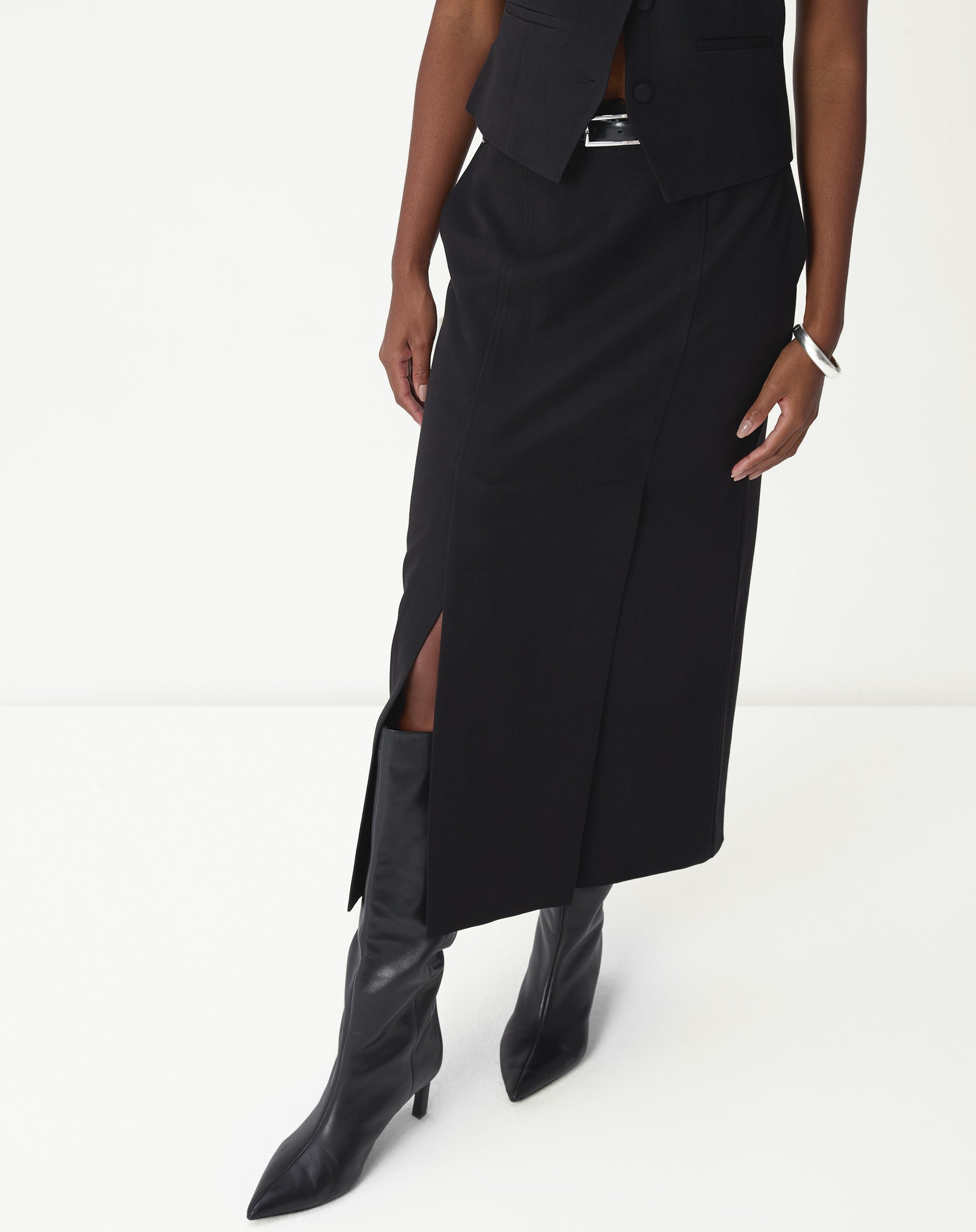 Detalhe da fenda lateral da saia midi preta mostrando abertura, caimento e bota cano alto.