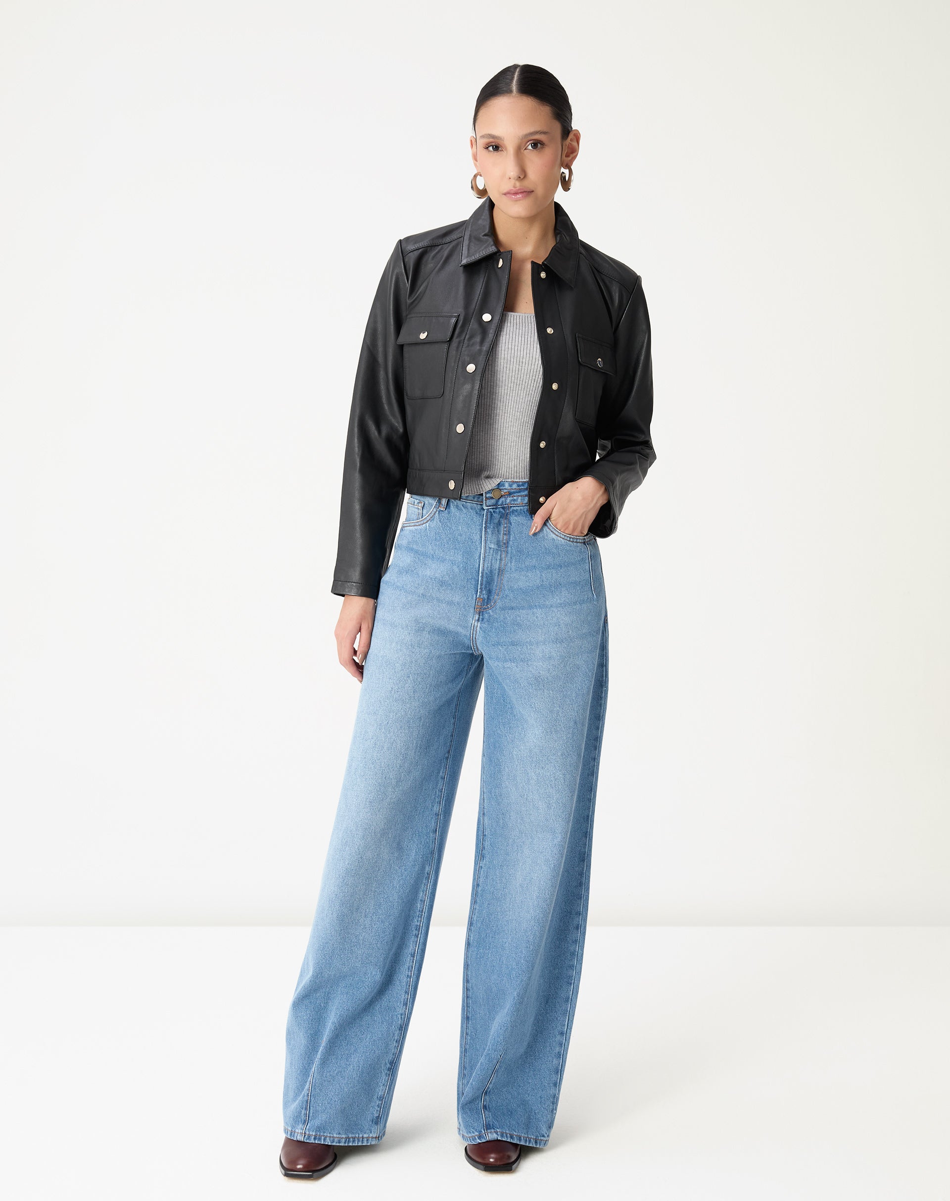 Vista completa da modelo usando jaqueta de couro preta curta com jeans de lavagem clara, look urbano e moderno