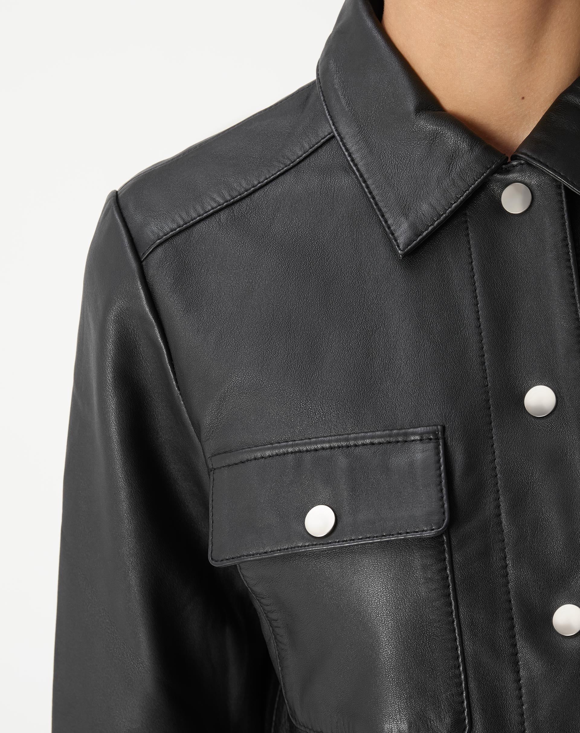 Close do ombro e manga da jaqueta de couro preta evidenciando costuras e textura do couro