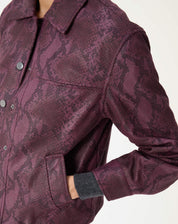 Enfoque no ombro e na manga da jaqueta cobra em PU vinho com costura estruturada e acabamento texturizado.