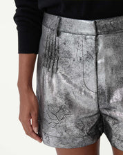 Close frontal do shorts metalizado prata mostrando pregas frontais, cós médio e bolso lateral em acabamento metalizado