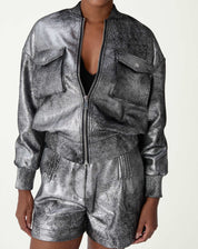 Modelo vestindo jaqueta bomber prata em suedine poliéster, vista frontal curta com zíper parcialmente aberto e shorts prateados combinando