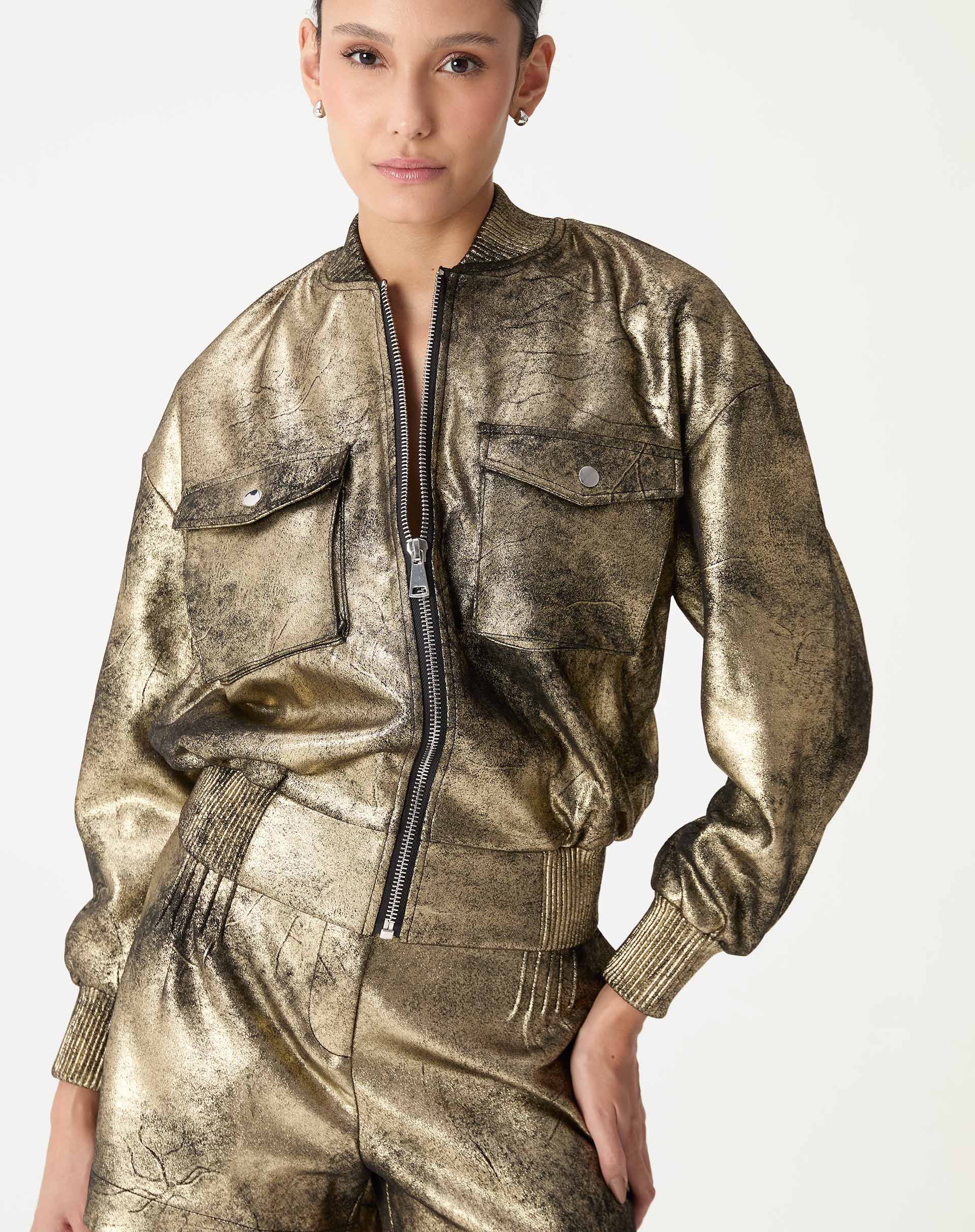 Jaqueta bomber dourada em suedine, modelo vestindo look coordenado com shorts metálicos, vista frontal mostrando zíper e gola canelada