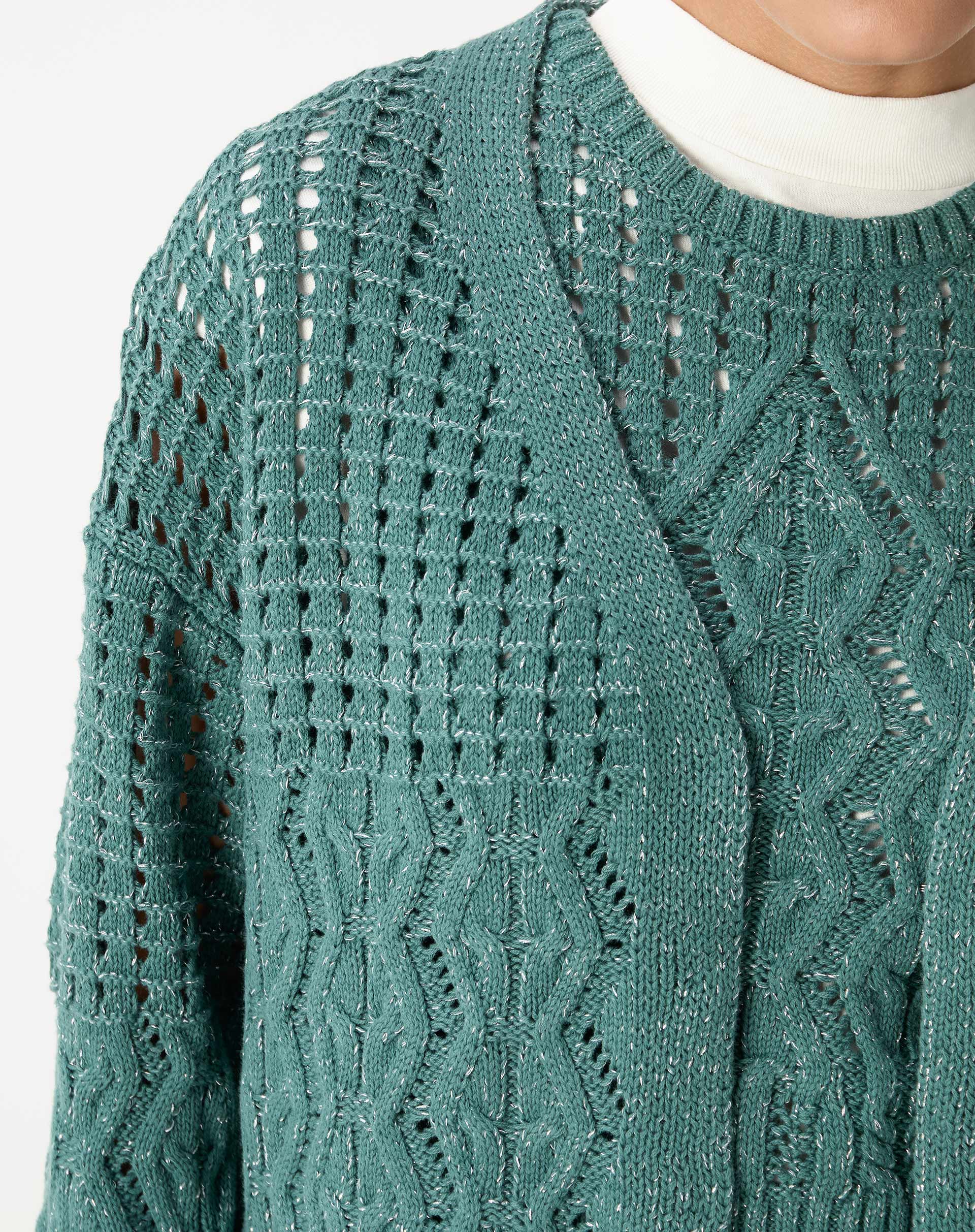 Detalhe do decote em V e corpo do cardigan de tricô verde com pontos abertos e faixa em tecido canelado no centro.
