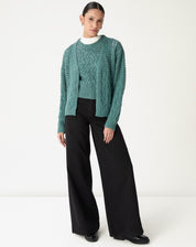 Modelo vestindo cardigan de tricô verde aberto sobre blusa branca e calça preta pantalona, mostrando o caimento e comprimento - cardigan longo verde.