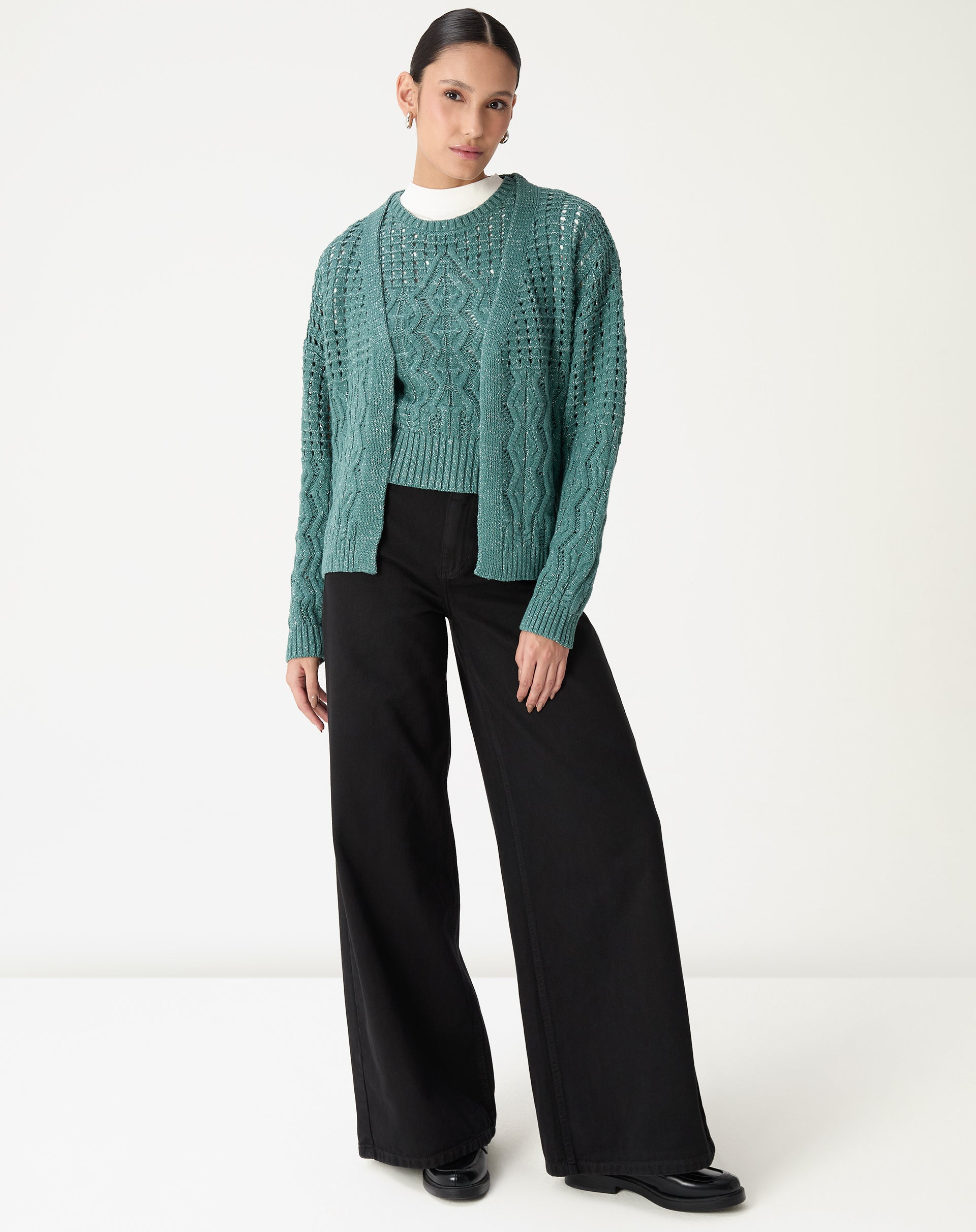 Modelo vestindo cardigan de tricô verde aberto sobre blusa branca e calça preta pantalona, mostrando o caimento e comprimento - cardigan longo verde.