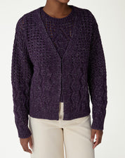 Close-up do decote V e abertura frontal do cardigan tricot roxo em fundo branco, mostrando a trama do ponto.