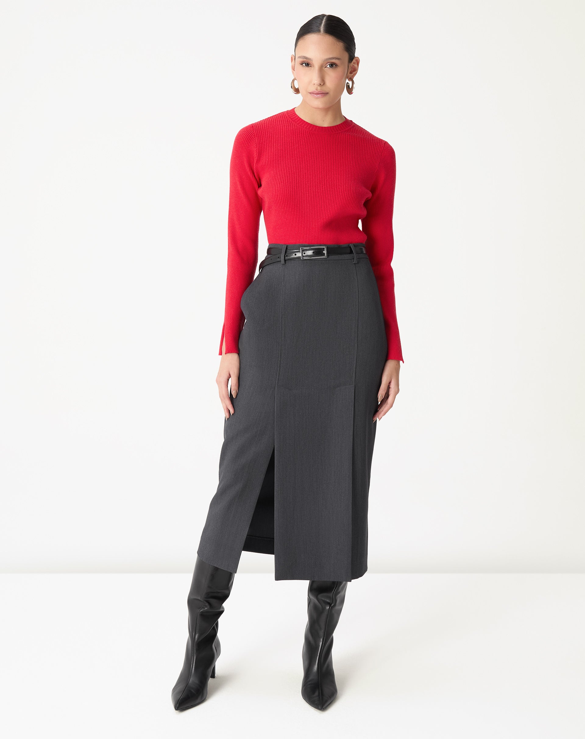 Modelo inteiro com suéter vermelho combinando com saia midi cinza, cinto e botas pretas, estilo elegante.
