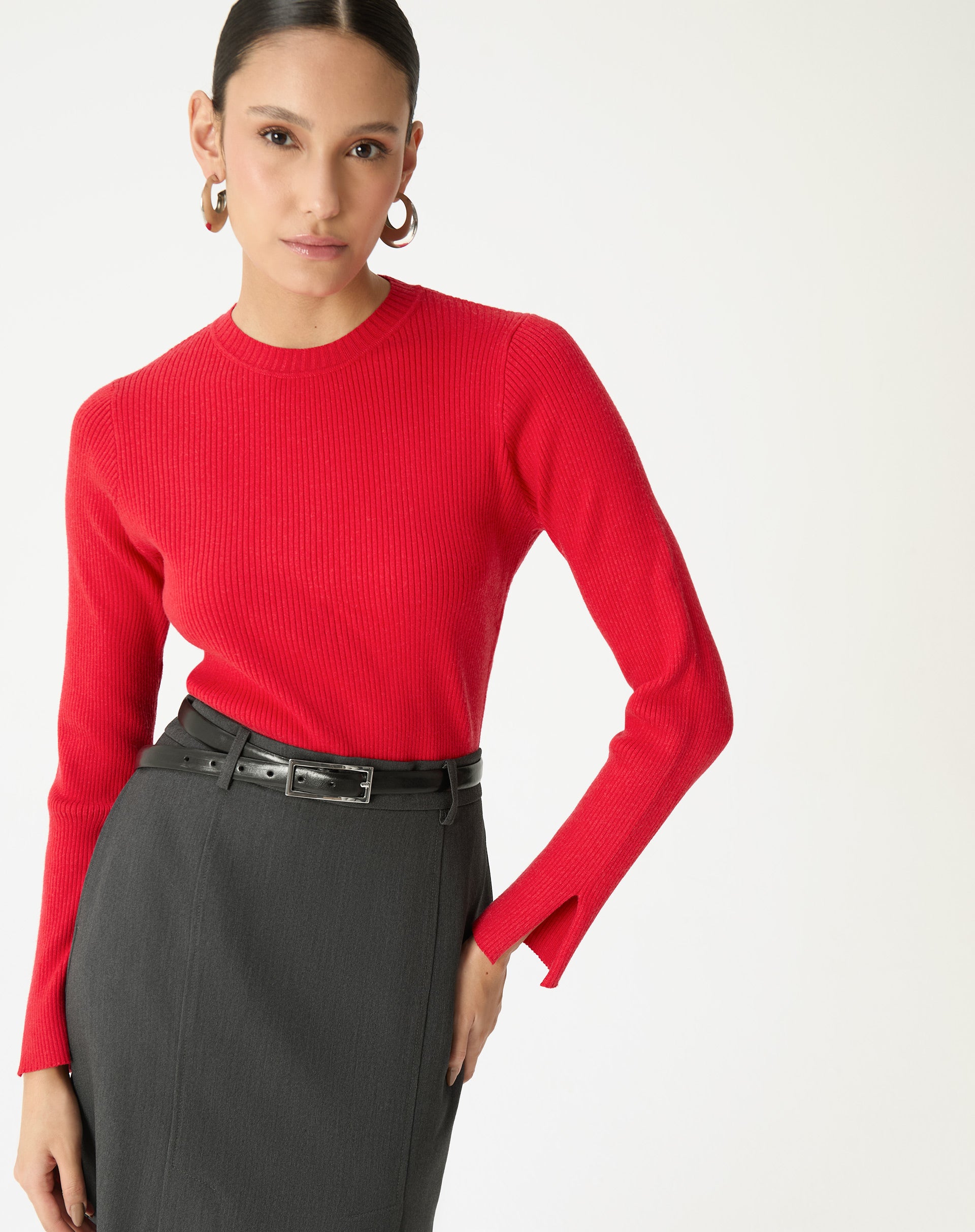 Modelo vestindo suéter vermelho de tricot com saia lápis cinza e cinto preto, destacando ajustada com mangas longas.