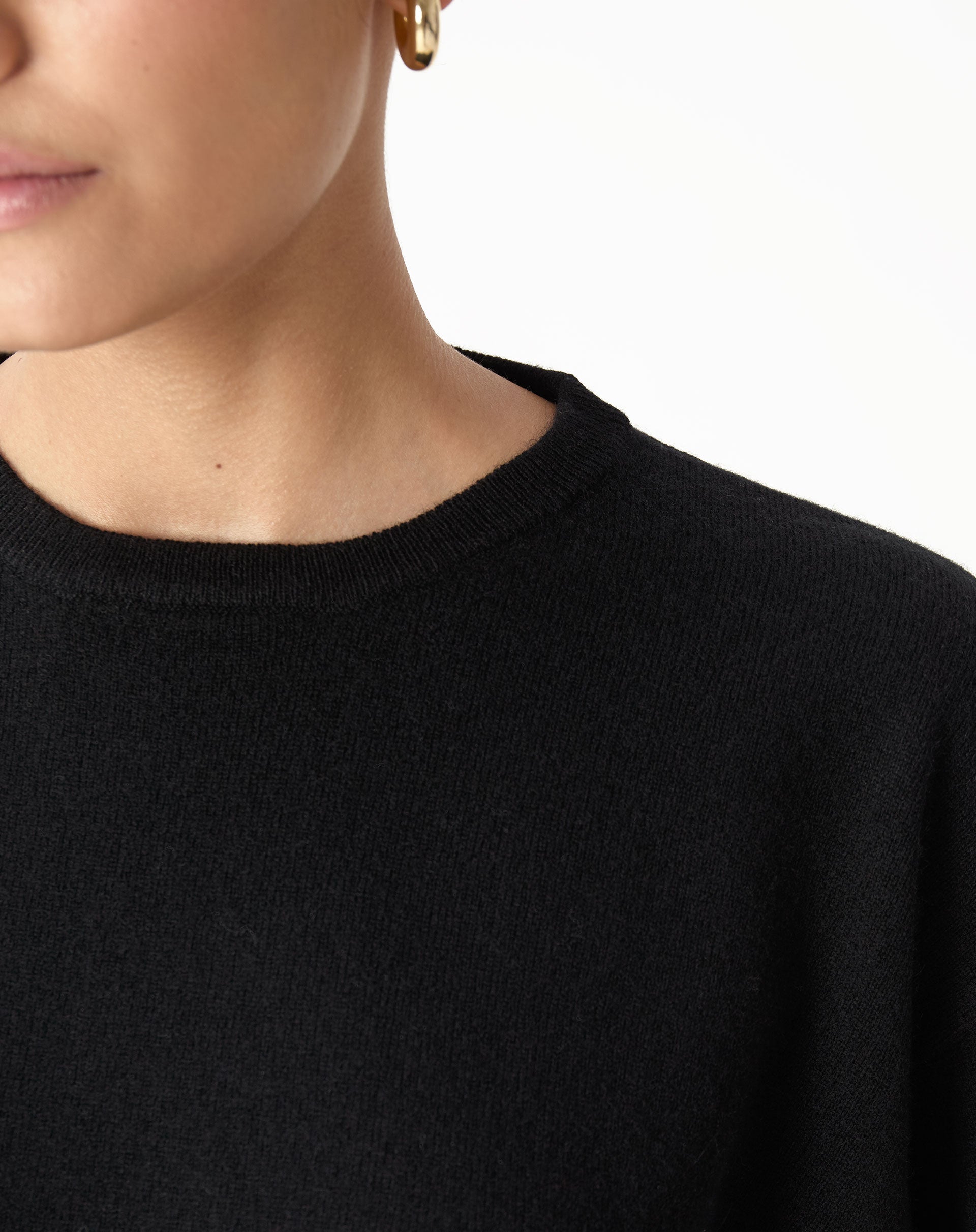 Detalhe do decote redondo (gola careca) do suéter em cashmere preto, acabamento discreto