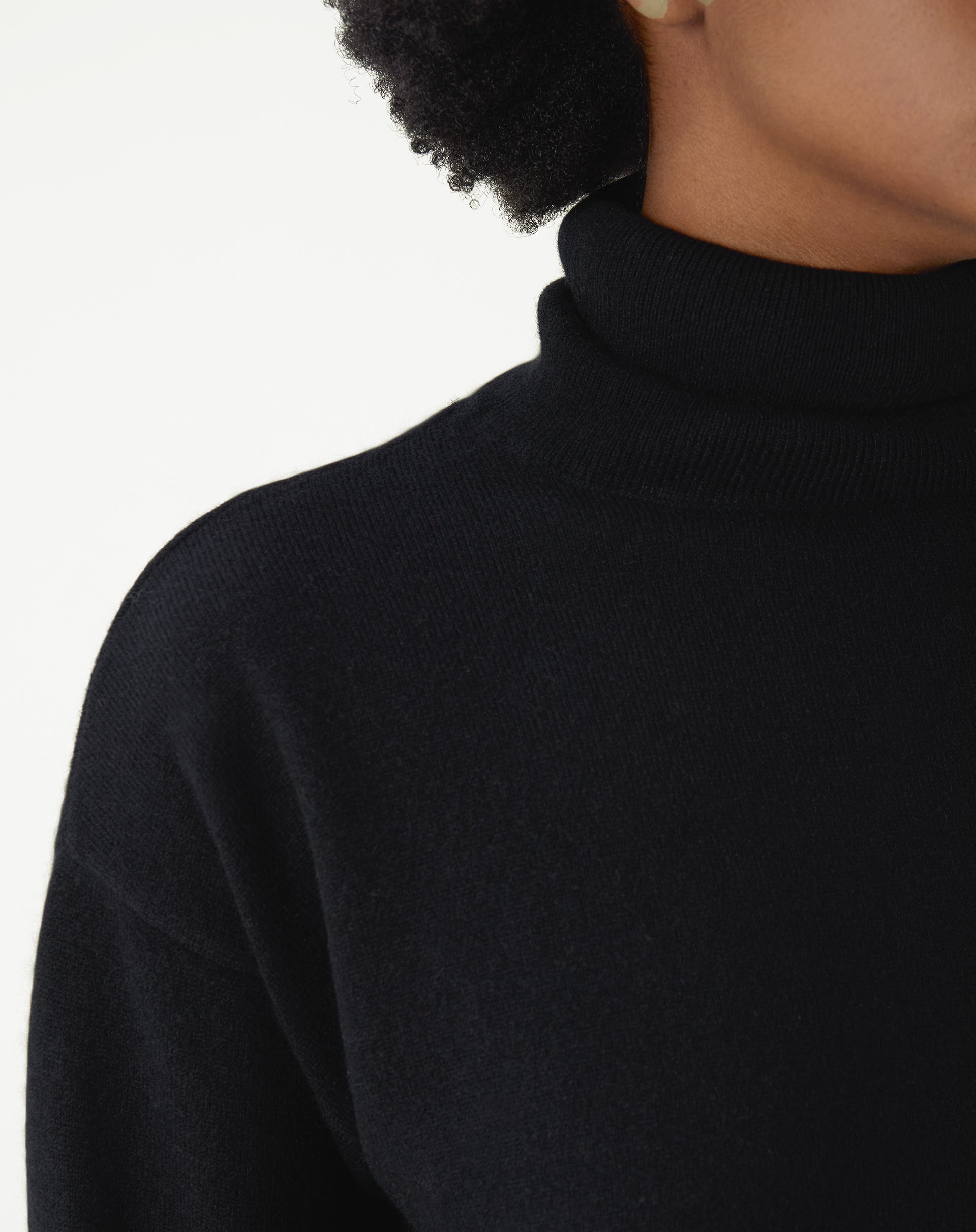 Detalhe frontal do suéter gola alta preto em tricot, evidenciando textura macia e acabamento liso da peça