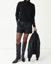 Modelo usando suéter gola alta em cashmere preto com shorts de couro e botas longas, look urbano e minimalista