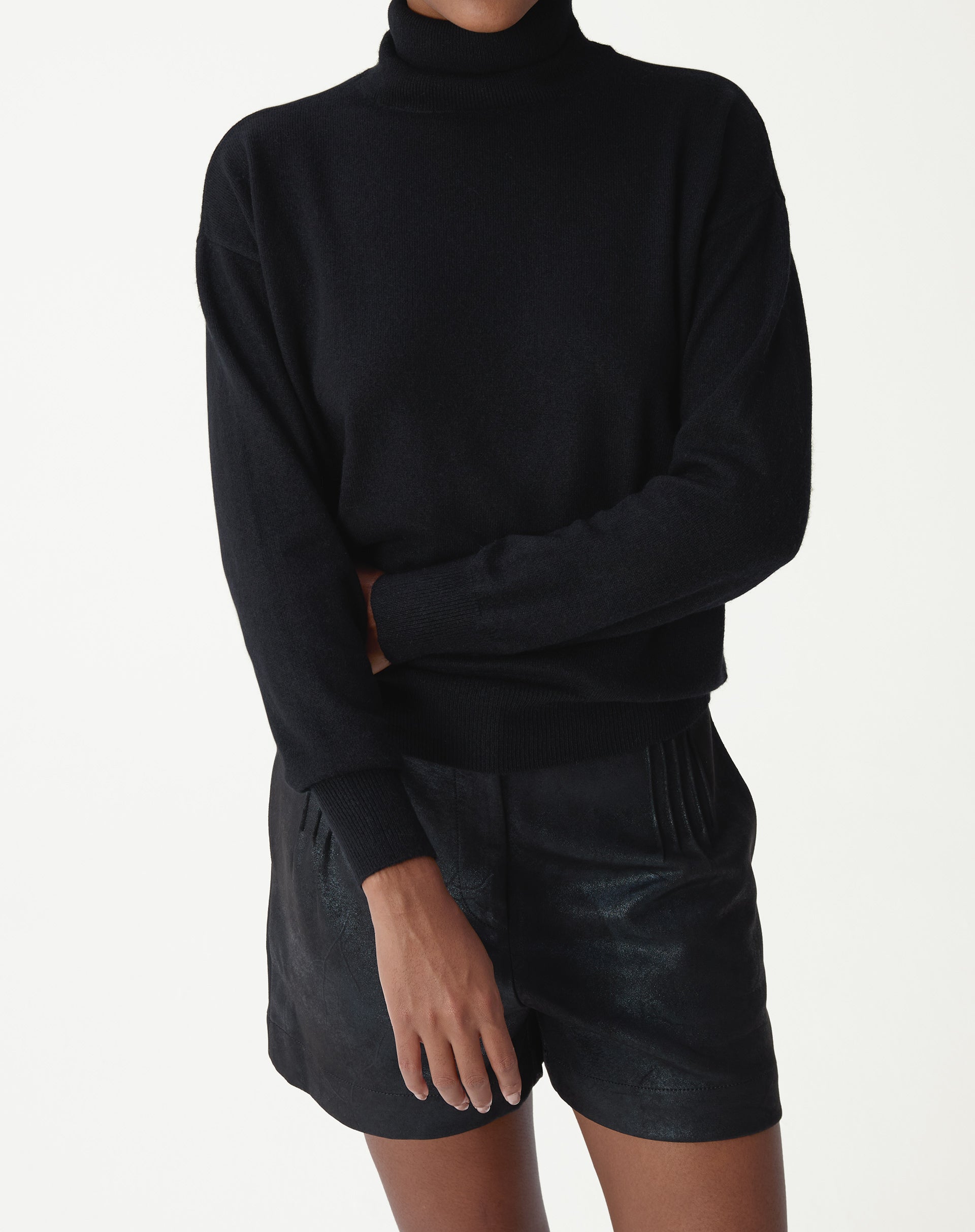 Vista traseira do suéter gola alta preto em tricot cashmere mostrando caimento quadrado e barra canelada sobre shorts de couro