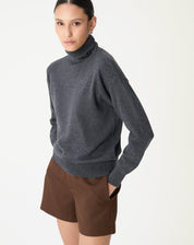 Modelo de lado vestindo um suéter de gola alta em cashmere cinza mescla escuro com um shorts marrom, caimento regular e estilo minimalista.