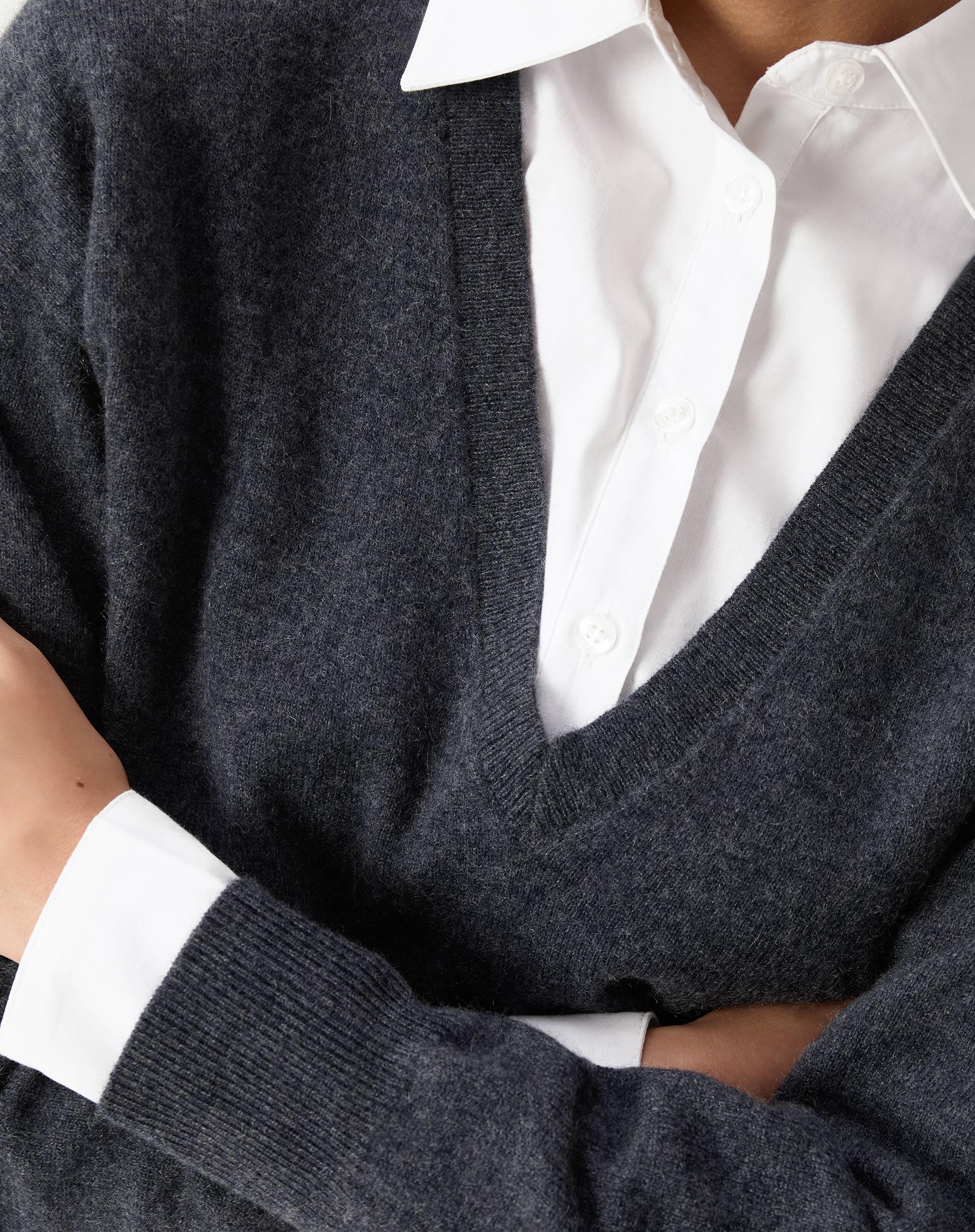 Vista do detalhe frontal do suéter, destacando a textura macia e acabamento impecável sobre camisa branca