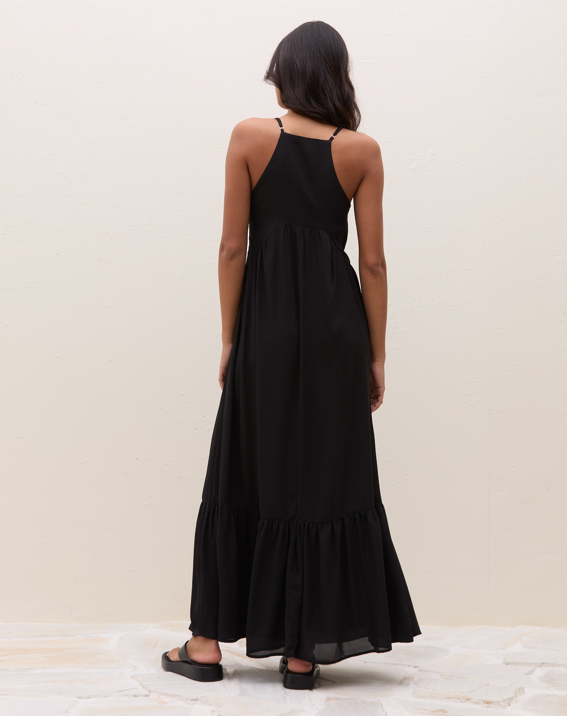 Vista frontal inteira do vestido maxi preto com alças finas, decote V, marcação abaixo do busto e barra com babado - look verão minimalista