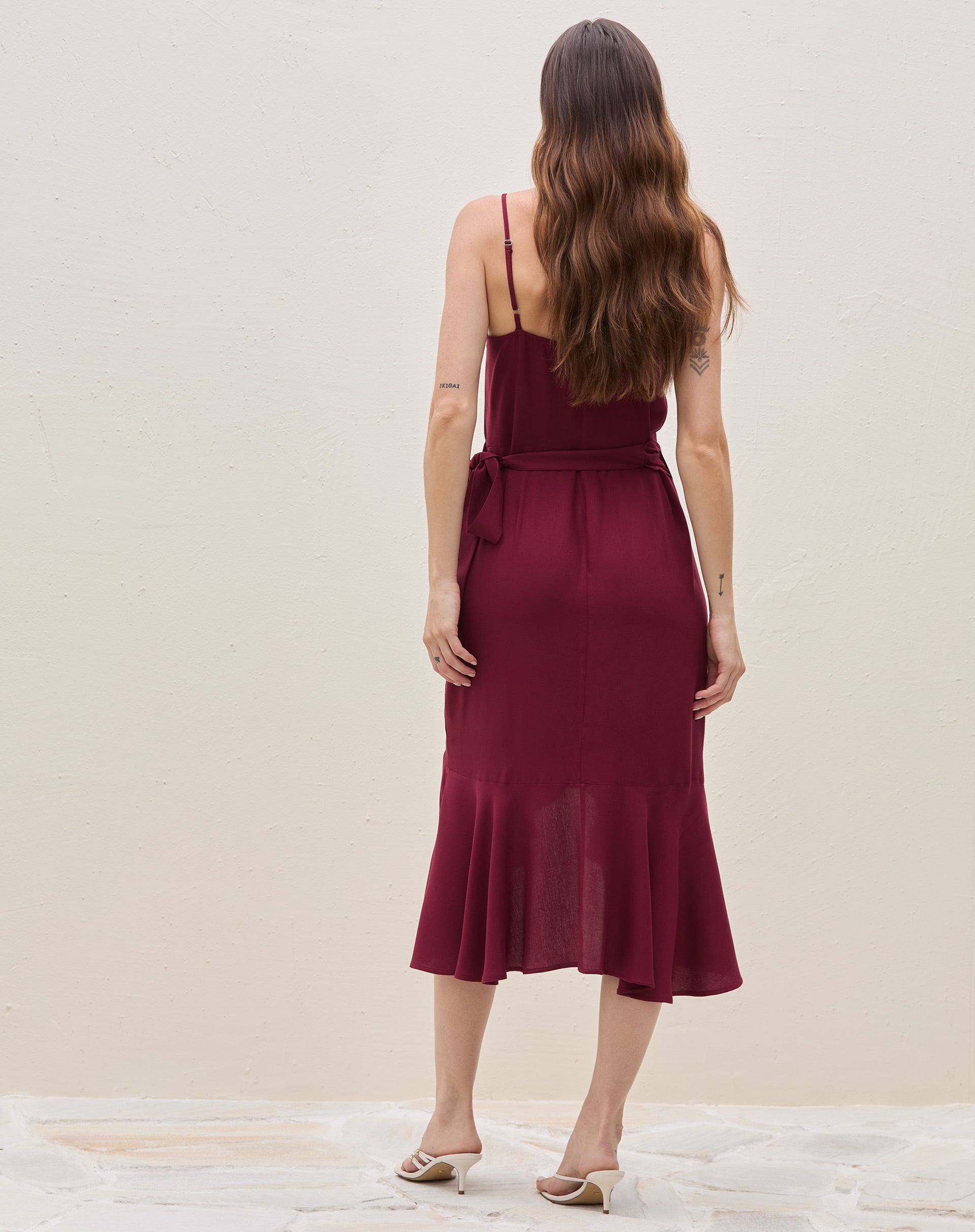 Detalhe frontal do babado assimétrico e da fenda envelopada do vestido midi transpassado vinho, evidenciando o movimento do tecido.