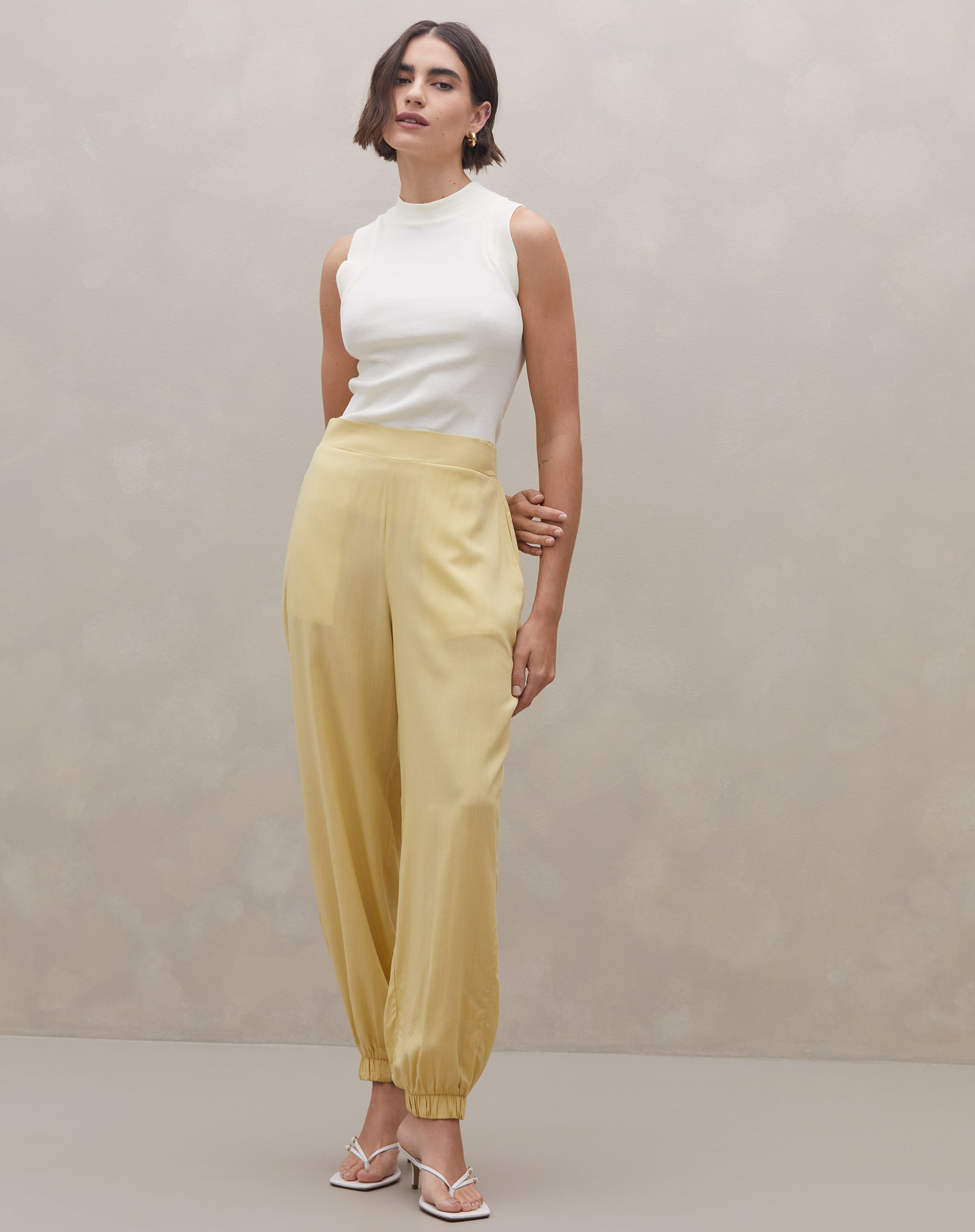 Modelo usando Calça Jogger Aladim cor manteiga em viscose lyocel, vista frontal com top branco e sandálias